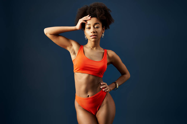 Femme afro-américaine élégante posant dans un bikini orange sur un fond bleu. - Photo, image