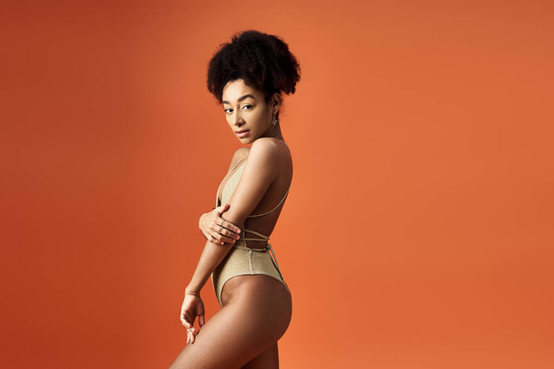 Elegante donna afroamericana che colpisce una posa in costume da bagno alla moda su sfondo arancione brillante. - Foto, immagini