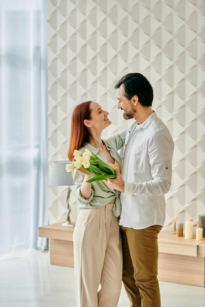 Eine rothaarige Frau und ein bärtiger Mann stehen in einem Raum voller Blumen und genießen die gemeinsame Zeit in einem modernen Ambiente.. - Foto, Bild