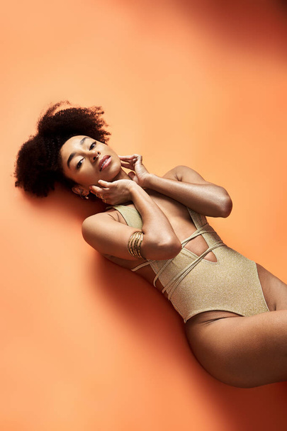 Stylish African American woman sunbathing in trendy swimsuit on bright orange background. - Photo, Image