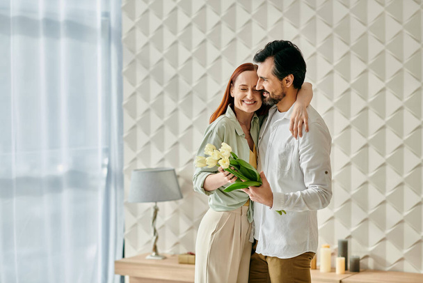Egy gyönyörű felnőtt pár, egy vörös hajú nő, és egy szakállas férfi egy intim pillanatban ölelkeznek a modern nappaliban.. - Fotó, kép