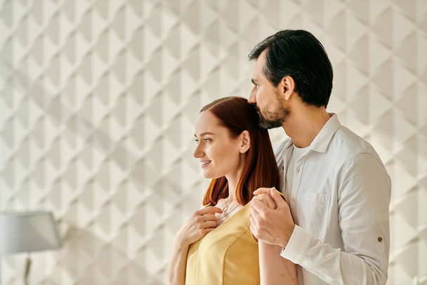 Şık bir yetişkin çift, kızıl saçlı bir kadın ve sakallı bir adam, minimalist beyaz bir duvarın önünde yan yana duruyorlar.. - Fotoğraf, Görsel
