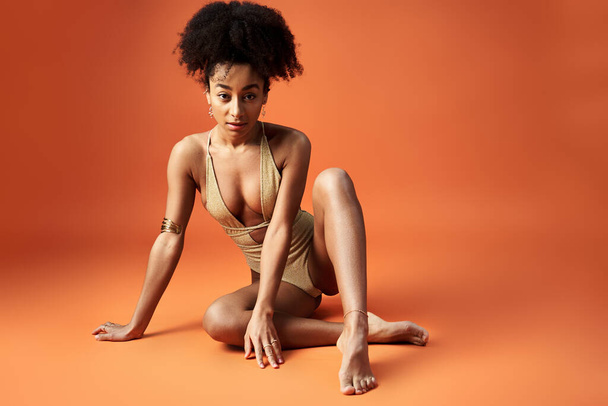 Elegante mujer afroamericana en bikini posando sobre fondo naranja brillante. - Foto, imagen