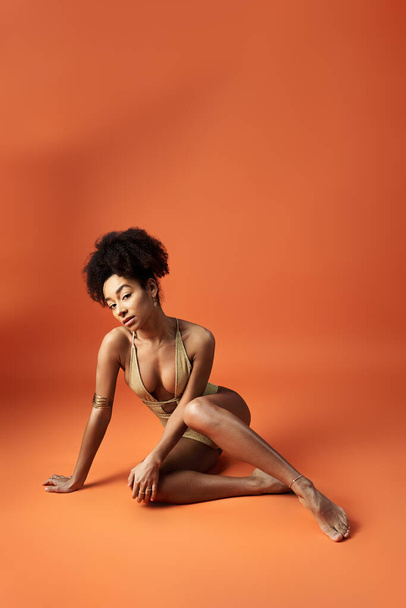 Привлекательная афроамериканка позирует в стильном бикини на ярком оранжевом фоне. - Фото, изображение