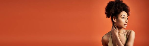 Stylová mladá Afroameričanka s kudrnatým účesem, která zaujme pózu na pulzujícím oranžovém pozadí. - Fotografie, Obrázek