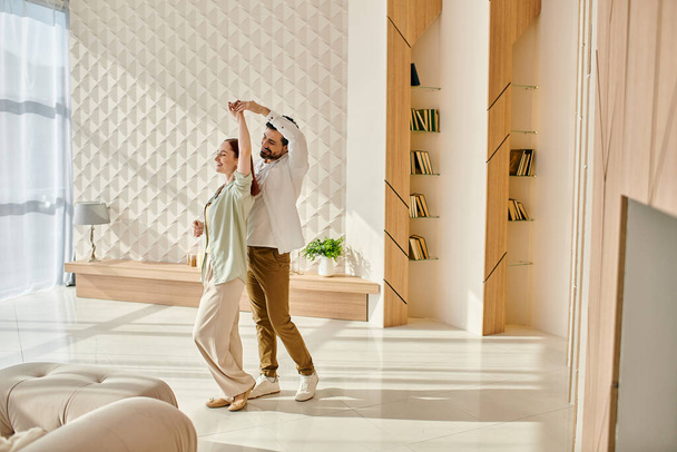Una bella coppia di adulti una donna rossa e un uomo barbuto danzano con grazia nei loro appartamenti moderni soggiorno. - Foto, immagini
