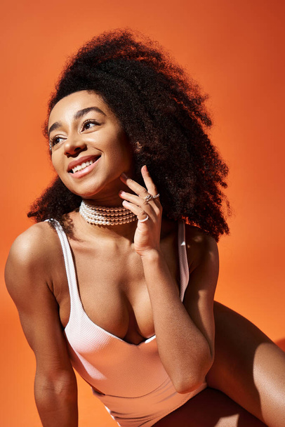 Stylish African American woman in white swimsuit poses on vibrant orange background. - Photo, Image