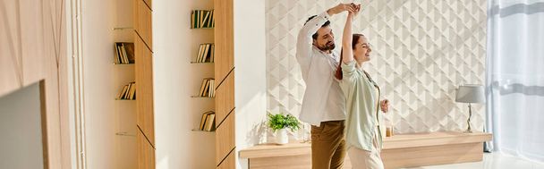Una hermosa pareja de adultos, una pelirroja y un hombre barbudo, bailando juntos en una moderna sala de estar. - Foto, imagen