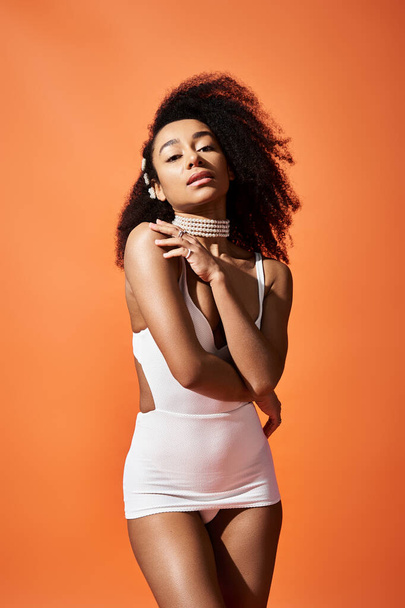Stylish African American woman strikes a pose in white swimsuit against vibrant orange backdrop. - Photo, Image