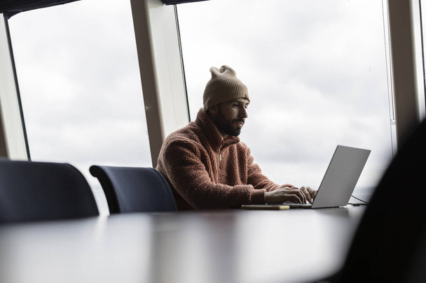 Jeunes professionnels masculins concentrés sur son ordinateur portable dans un bureau bien éclairé avec de grandes fenêtres. - Photo, image