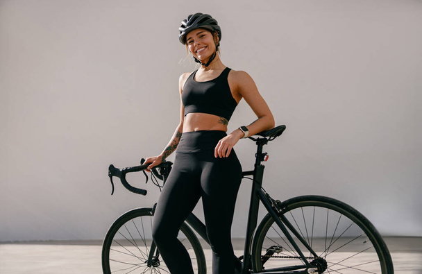 Mujer ciclista en equipo de protección de pie con su bicicleta mientras entrena al aire libre y se ve la cámara - Foto, Imagen
