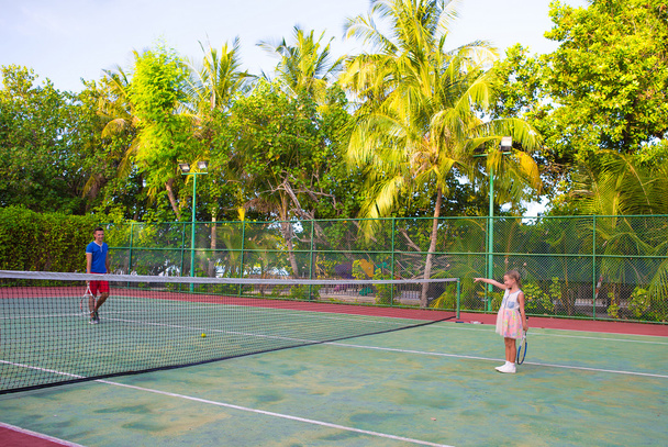 Niña jugando al tenis con su padre en la cancha
 - Foto, imagen