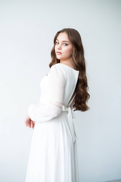 retrato de una joven con el pelo largo en un vestido blanco sobre un fondo gris - Foto, Imagen
