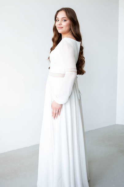 bonita mujer joven en vestido blanco con el pelo largo posando sobre un fondo blanco en el estudio - Foto, imagen