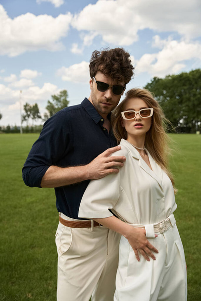 Un beau jeune couple, vêtu d'une tenue élégante, pose affectueusement dans un champ verdoyant sous le vaste ciel. - Photo, image
