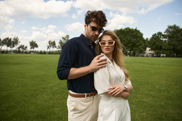 Un homme et une femme, élégamment habillés, se tiennent ensemble dans un champ verdoyant, incarnant une vie de luxe et de sophistication. - Photo, image