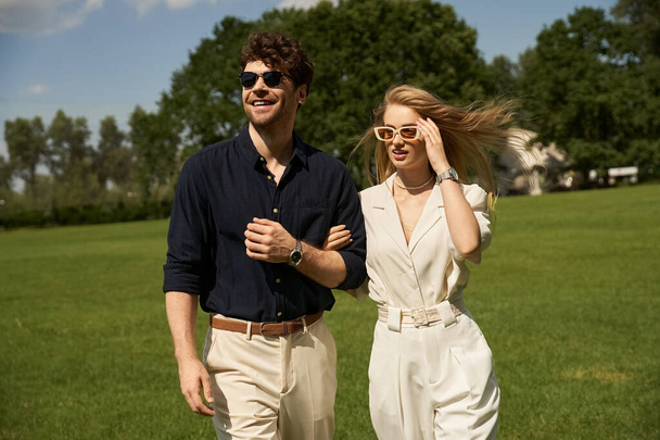 Una bella giovane coppia in abiti eleganti passeggia attraverso un lussureggiante campo verde in uno spettacolo di stile old-money e stile di vita ricco. - Foto, immagini