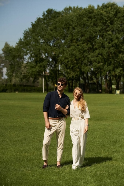 Красивая молодая пара в элегантной одежде стоит вместе на пышном зеленом поле, воплощая в себе роскошный образ жизни старого мира. - Фото, изображение