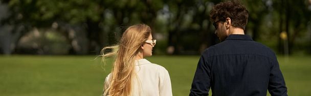 Egy gyönyörű, elegáns ruhás fiatal pár sétál át egy zöld parkon, régi pénzstílust árasztva és gazdag emberek életét élve.. - Fotó, kép