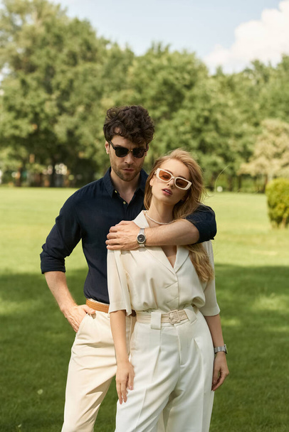 Элегантная пара, одетая в стильный наряд, позирует на открытом воздухе в парке на пышной зеленой траве. Принять образ жизни богатых людей. - Фото, изображение