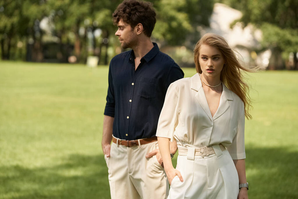 Krásný, stylový mladý pár v elegantním oblečení kráčející spolu v bujném zeleném parku naplněném pulzujícím listím. - Fotografie, Obrázek