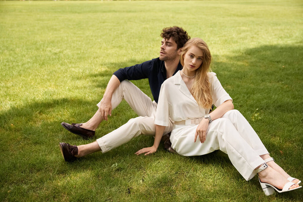 Стильна молода пара в елегантному вбранні відпочиває на пишній зеленій траві, занурюючись один в одного компанія - Фото, зображення