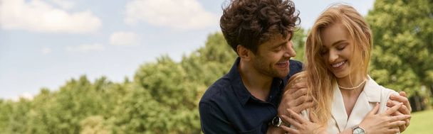 Ένα κομψό νεαρό ζευγάρι, ντυμένο με κομψή ενδυμασία, αγκαλιάζει ο ένας τον άλλον σε ένα καταπράσινο χώρο, εκφράζοντας αγάπη και σύνδεση. - Φωτογραφία, εικόνα