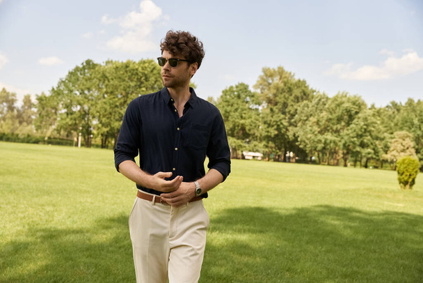 Mężczyzna w niebieskiej koszuli i brązowych spodniach spokojnie spaceruje po bujnym zielonym polu pod rozległym otwartym niebem. - Zdjęcie, obraz