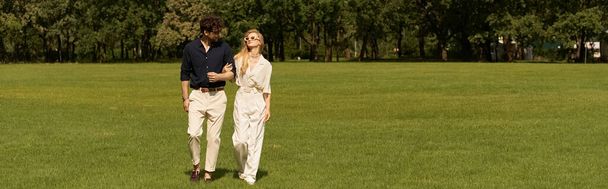 Мужчина и женщина в элегантной одежде стоят вместе на пышном зеленом поле, воплощая щедрый и изысканный образ жизни. - Фото, изображение