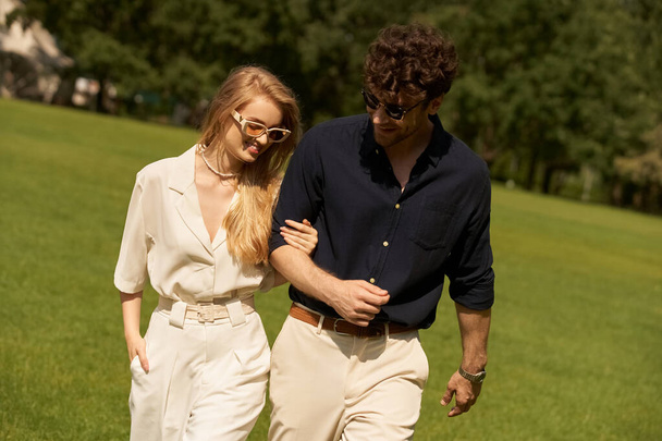 Egy gyönyörű fiatal pár, elegánsan öltözve, kényelmesen sétálnak a parkban a zöld mezőn.. - Fotó, kép