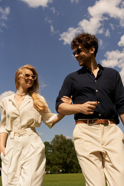 Elegante coppia con vecchio stile denaro godendo di una piacevole passeggiata attraverso un vasto campo verde sotto il cielo. - Foto, immagini