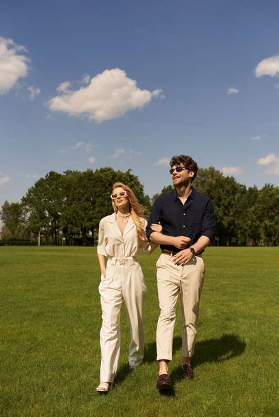An elegant couple leisurely walks together through a lush green field, exuding old-money sophistication and luxury. - Photo, Image