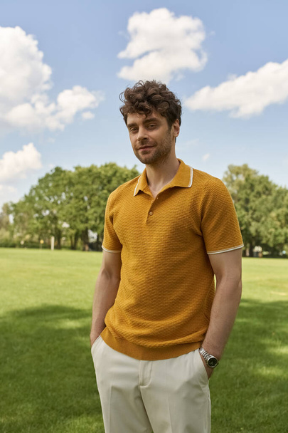 Мужчина в желтой рубашке для поло уверенно стоит среди пышной зелени поля. - Фото, изображение