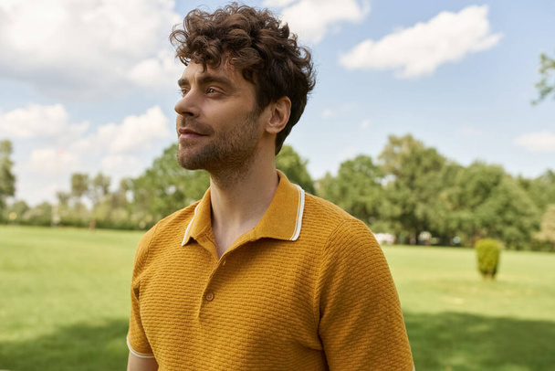 Um homem, vestido com uma camisa amarela vibrante, está confiante em um vasto campo cheio de vegetação exuberante sob o brilho quente sóis. - Foto, Imagem