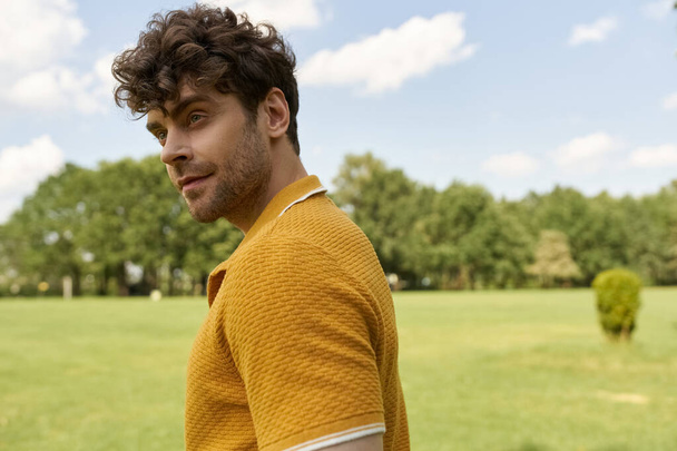 Un uomo in camicia gialla si trova fiducioso in un vasto campo verde. - Foto, immagini
