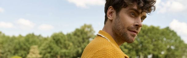 Um homem com uma camisa amarela olha com confiança para longe em um ambiente ao ar livre, exalando estilo e carisma. - Foto, Imagem