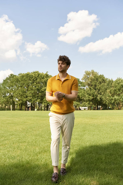 Canlı sarı tişörtlü şık bir adam çimenli bir tarlanın yemyeşil bahçesinde zarif bir şekilde duruyor.. - Fotoğraf, Görsel