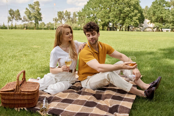豪華で洗練されたライフスタイルを体現し,緑豊かな公園のフィールドでピクニックを楽しむエレガントな服装のスタイリッシュな若いカップル. - 写真・画像