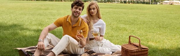 Elegant couple in stylish attire enjoying a leisurely moment on a picnic blanket amidst a lush park setting. - Photo, Image