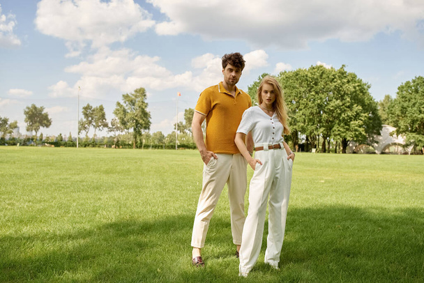 Un beau jeune couple, vêtu élégamment, debout ensemble dans un champ verdoyant, exsudant un sentiment de luxe riche de vieil argent. - Photo, image