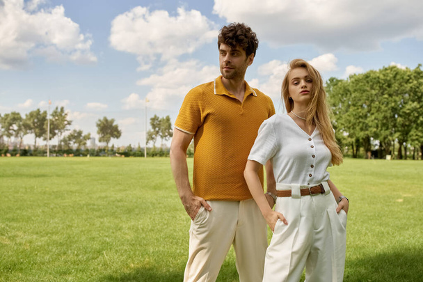 Ein schönes junges Paar in eleganter Kleidung steht auf einem saftig grünen Feld und verströmt einen Hauch von Raffinesse und Anmut. - Foto, Bild