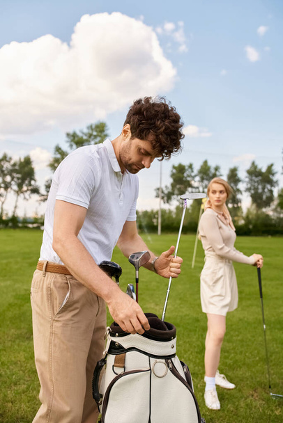 Ένας άντρας και μια γυναίκα με κομψή ενδυμασία στέκονται κοντά σε ένα καταπράσινο γήπεδο γκολφ, απολαμβάνοντας μια στιγμή συντροφικότητας.. - Φωτογραφία, εικόνα