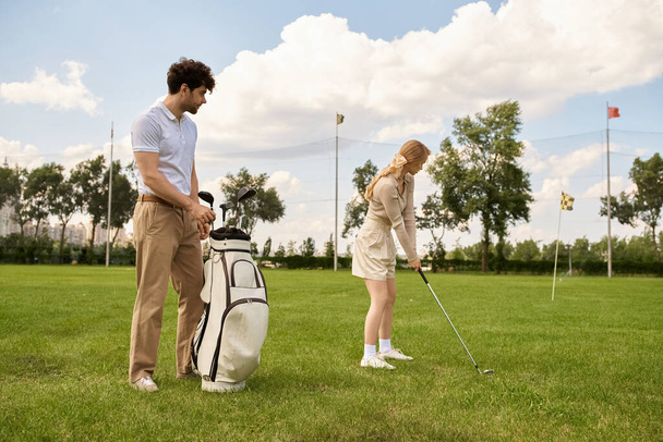 Ein junges Paar in eleganter Kleidung spielt Golf auf einer grünen Wiese in einem renommierten Club und genießt einen gemütlichen Tag zusammen. - Foto, Bild