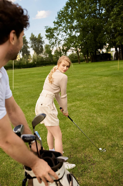 Mężczyzna i kobieta w eleganckim stroju grać w golfa na bujnym polu, pokazując swoje umiejętności, jak cieszyć się grą. - Zdjęcie, obraz