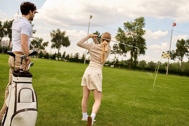 Ein Mann und eine Frau in eleganter Kleidung genießen eine Runde Golf auf einer grünen Wiese, umgeben von der Gelassenheit eines renommierten Golfclubs. - Foto, Bild