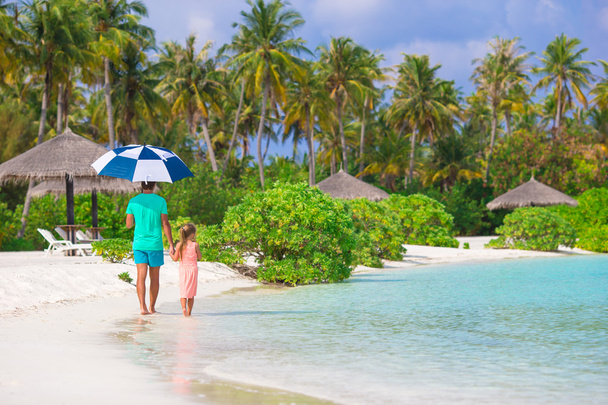 Отец и маленькая девочка с зонтиком прячутся от солнца на пляже
 - Фото, изображение