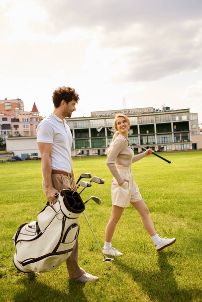 A man and woman in elegant attire walking casually on a grassy field with golf clubs in hand. - Photo, Image
