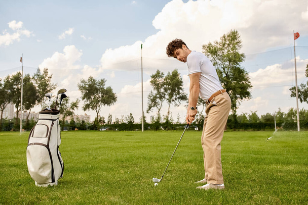 Mężczyzna ubrany w eleganckie ubrania uderza piłkę golfową na bujnym zielonym polu w klubie golfowym. - Zdjęcie, obraz