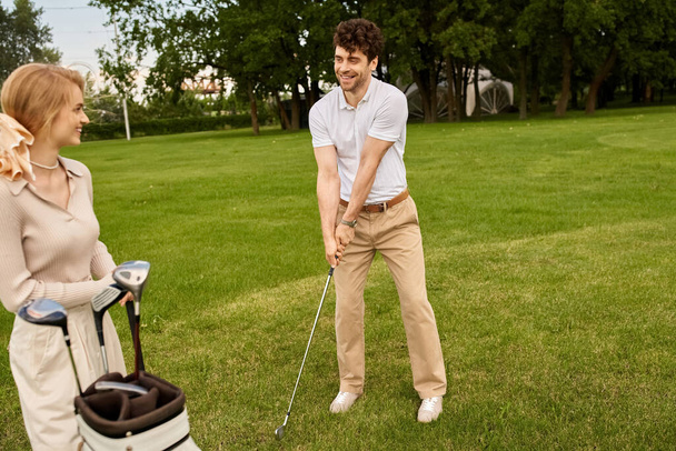 Een jong koppel, elegant gekleed, genieten van een potje golf op een weelderig groen veld bij een prestigieuze golfclub. - Foto, afbeelding