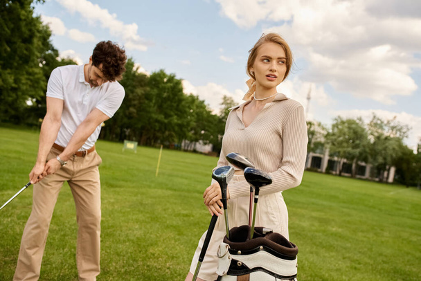 Młoda para w eleganckim stroju grająca razem w golfa na zielonym polu w prestiżowym klubie, ucieleśniająca elegancki styl życia. - Zdjęcie, obraz